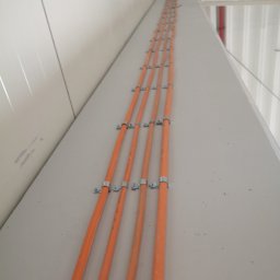 PRO-Elektro Serhii Kopylov - Pomarańczowe rury ułożone równolegle, przymocowane metalowymi uchwytami do jasnej ściany wzdłuż sufitu, widok z dołu.