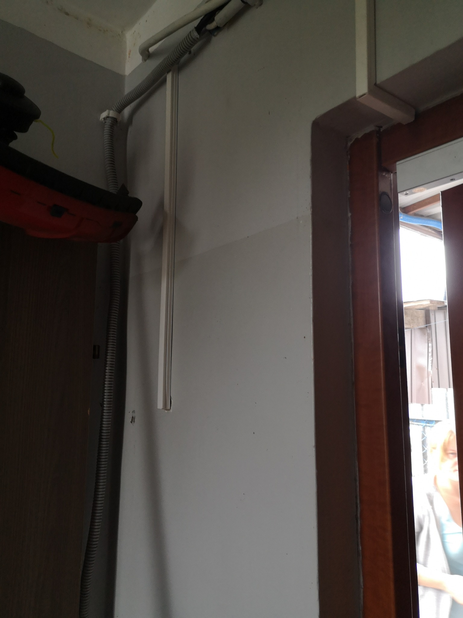 Szara rura karbowana i biała listwa przymocowane do ściany w pobliżu framugi drzwi, widoczne elementy instalacji elektrycznej.