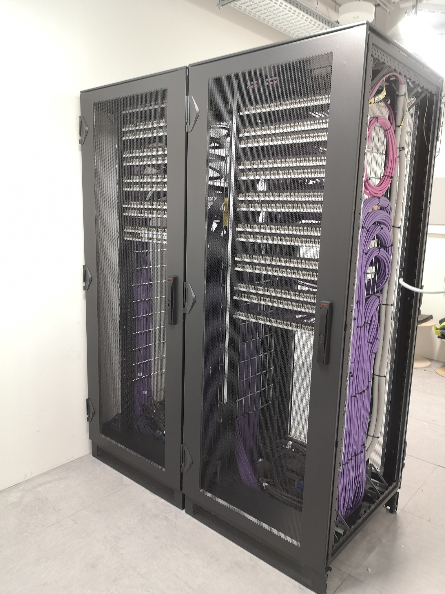 Dwie szafy serwerowe z okablowaniem w kolorze fioletowym i szarym, zainstalowane w pomieszczeniu w Pruszkowie. Widoczne kable uporządkowane wewnątrz i na zewnątrz szaf.