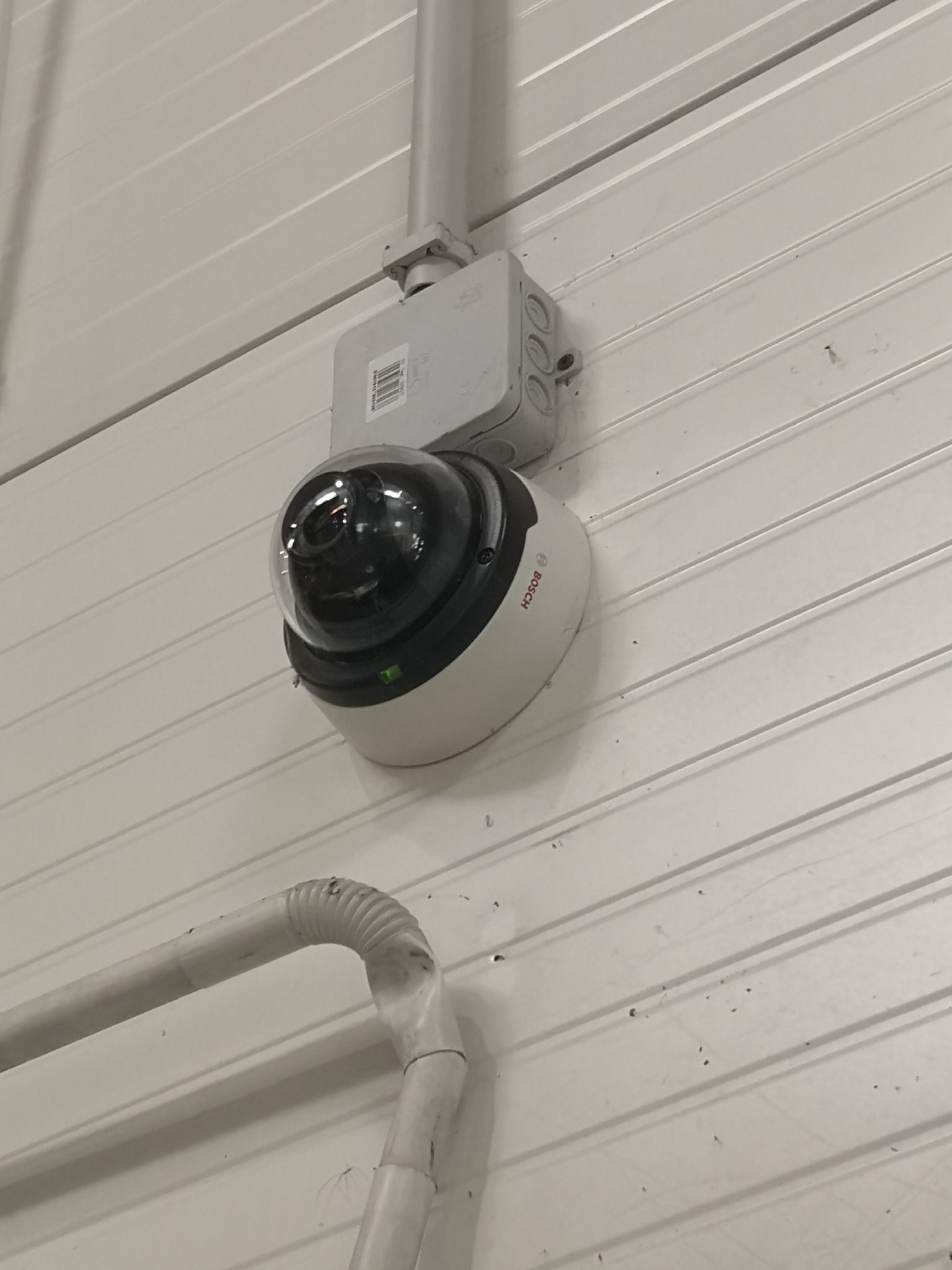 Kopułkowa kamera Bosch zamontowana na metalowej ścianie, widoczna puszka instalacyjna i rurka osłonowa przewodu.