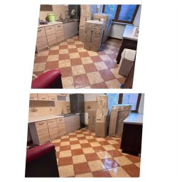 LAVIAN - Kartonowe pudła, owinięte folią stretch, ustawione w kuchni z brązowo-beżową szachownicą na podłodze, obok jasnych szafek i okna z widokiem na drzewa.