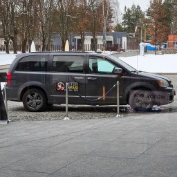 TAXI SEROCK MITER - Taksówka 24h - Postój Taxi - Szary minivan z logo 'MITER TAXI' zaparkowany przed budynkiem, odgrodzony ozdobnymi słupkami z liną.