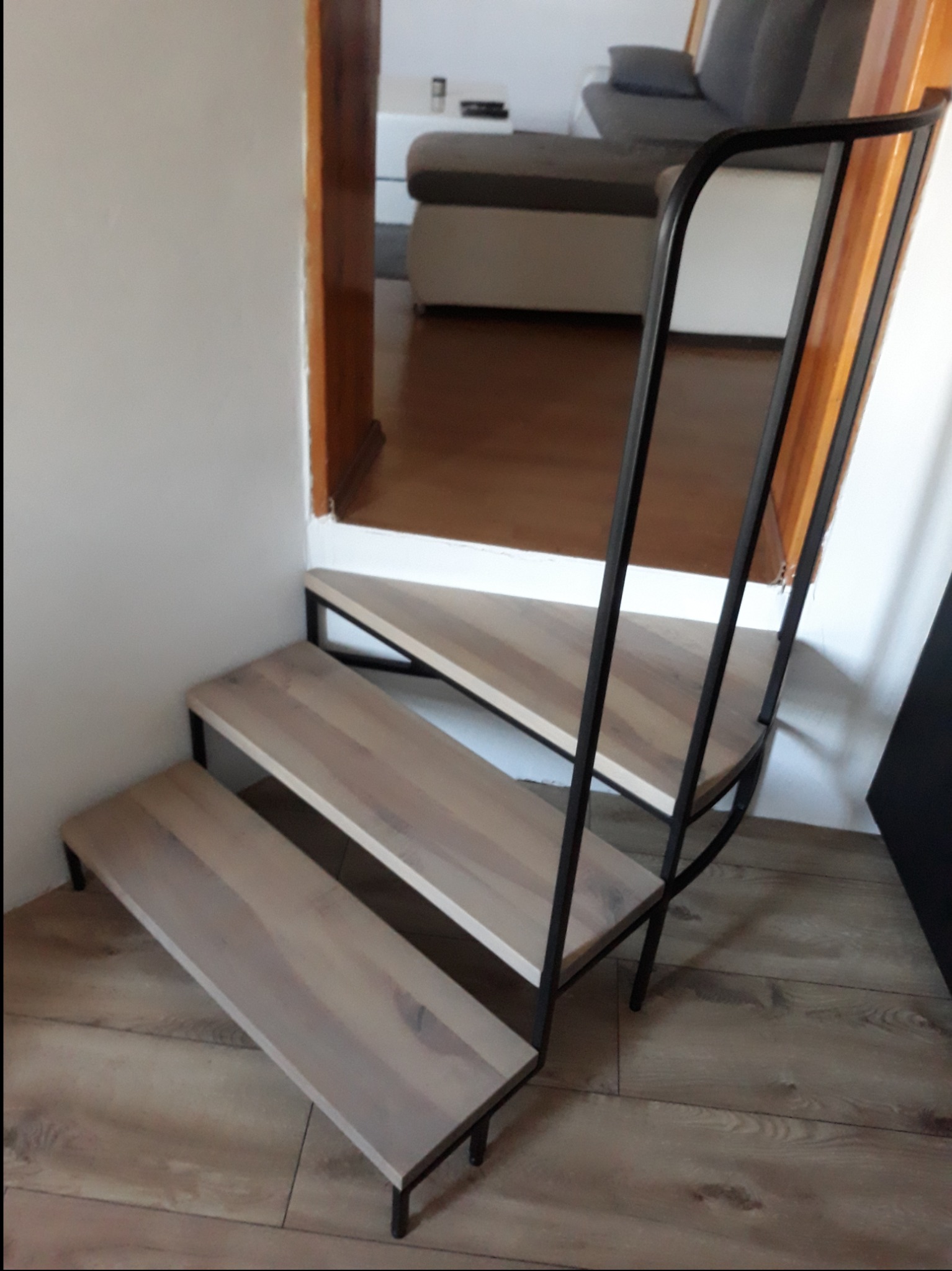 Metalowa konstrukcja schodów z drewnianymi stopniami, nowoczesny design, widok z dołu, widoczne elementy mocowania do ściany.