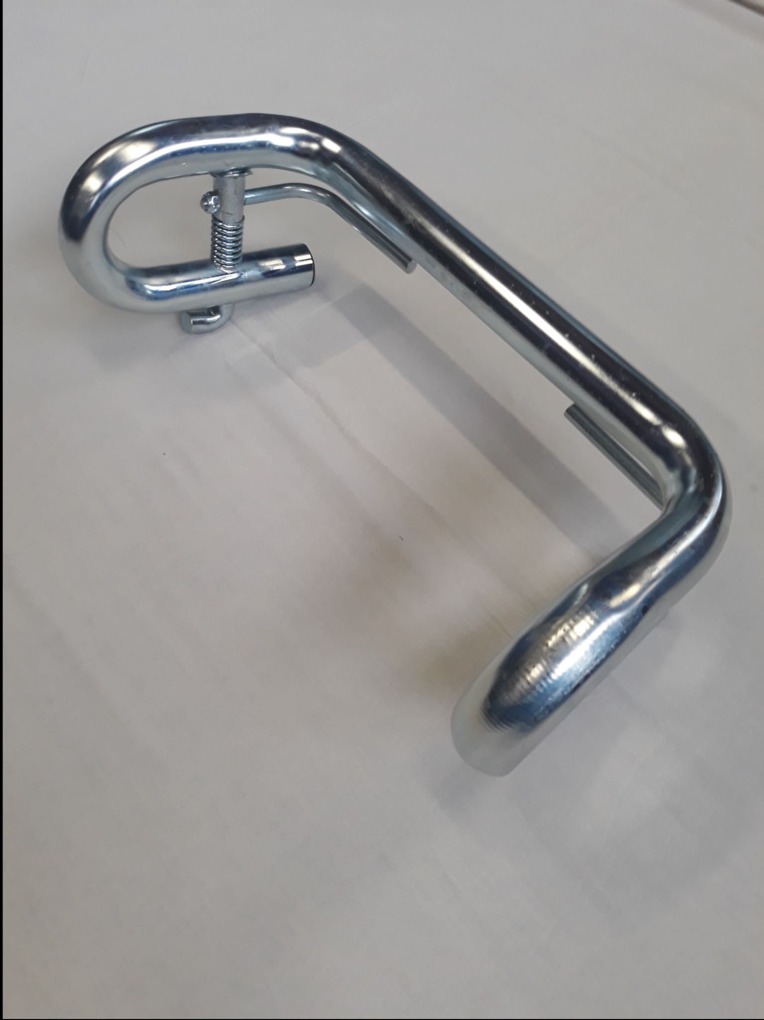 Chromowana, gięta rura z mechanizmem sprężynowym, prawdopodobnie element balustrady lub poręczy, leżąca na jasnej powierzchni.