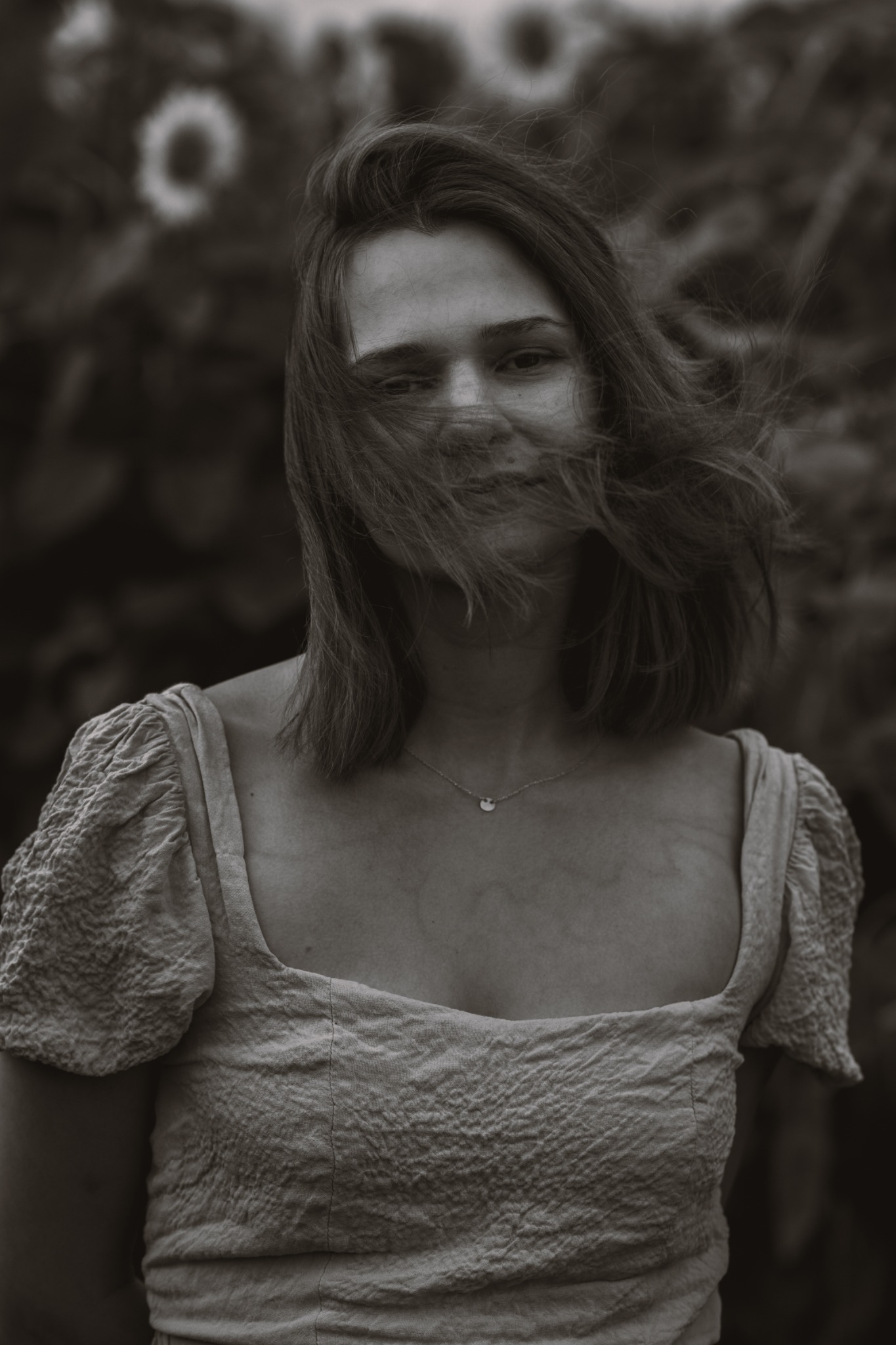 Portret kobiety w sukience z falującymi włosami na tle łąki zrobiony w Poznaniu, w stylu vintage.