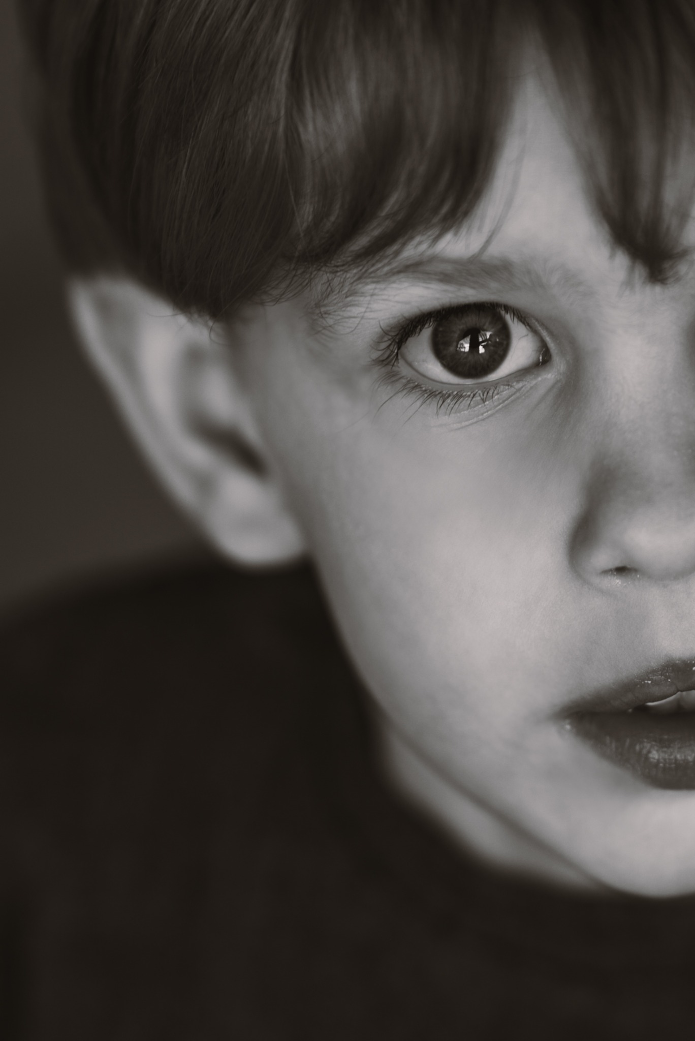 Czarno-białe, portretowe zbliżenie twarzy dziecka, z wyraźnym odbiciem w oku i lekko otwartymi ustami, skierowanymi w stronę światła.
