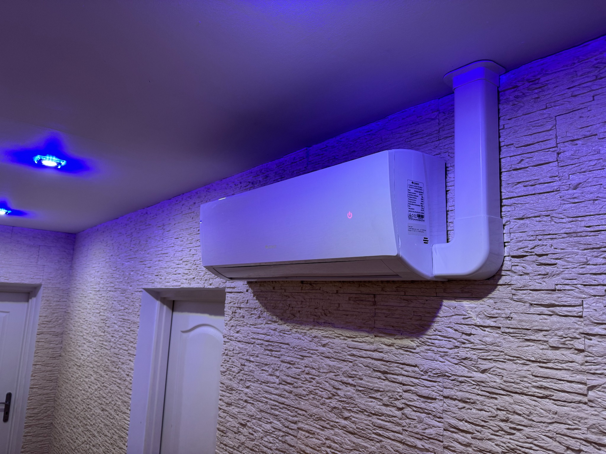 Zamontowany klimatyzator marki Gree na dekoracyjnej ścianie w pomieszczeniu w Krakowie, widoczne białe drzwi po lewej stronie, oświetlenie punktowe w suficie.