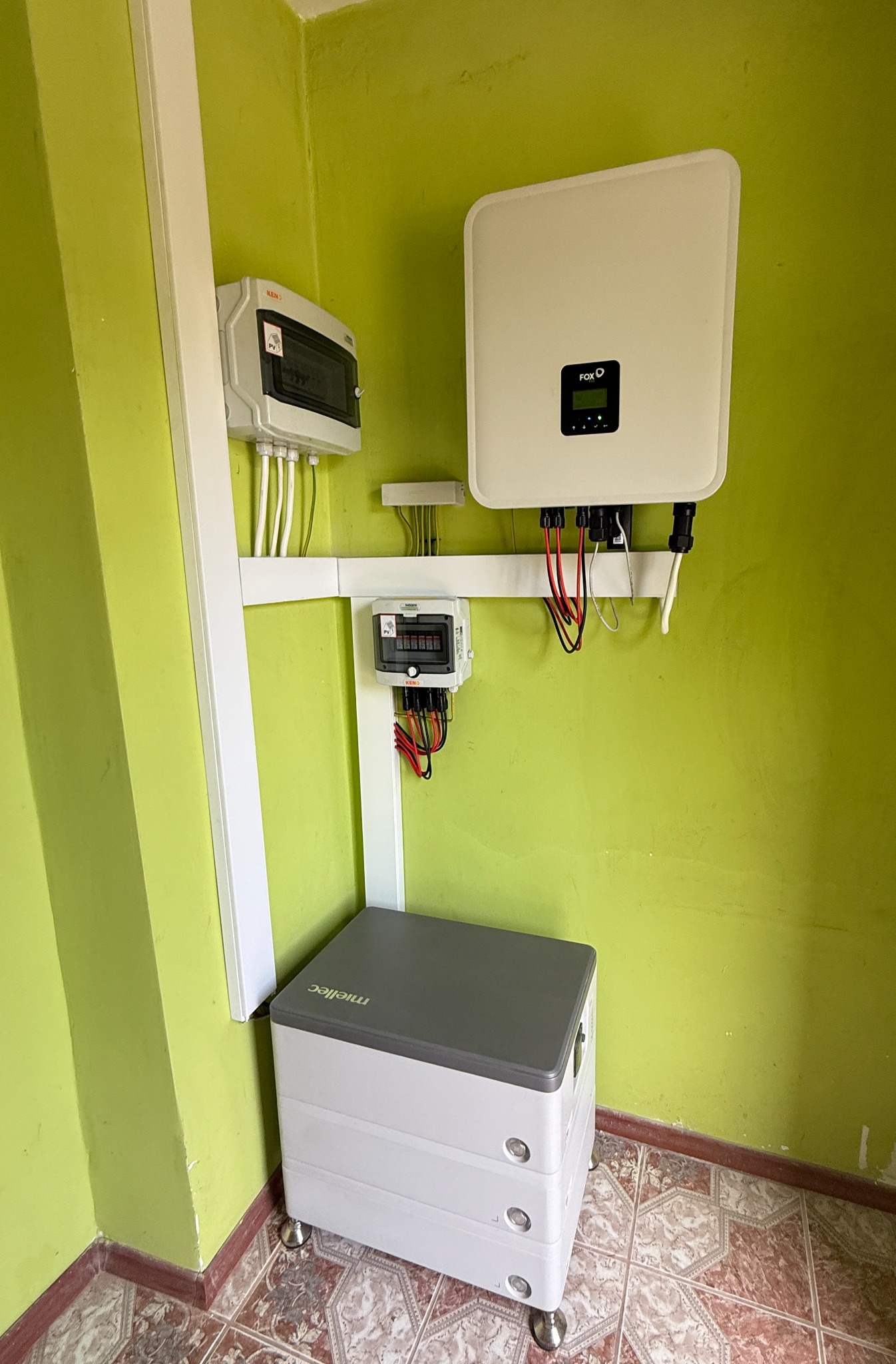 Zamontowany inwerter FOX D i magazyn energii Mielec na tle zielonej ściany i wzorzystej podłogi. Widoczne kable i zabezpieczenia instalacji fotowoltaicznej.