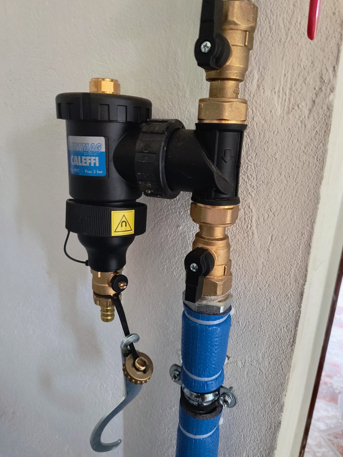 Zamontowany filtr magnetyczny Caleffi z zaworami na rurze w instalacji grzewczej, widoczne złącza i niebieska izolacja termiczna rury.