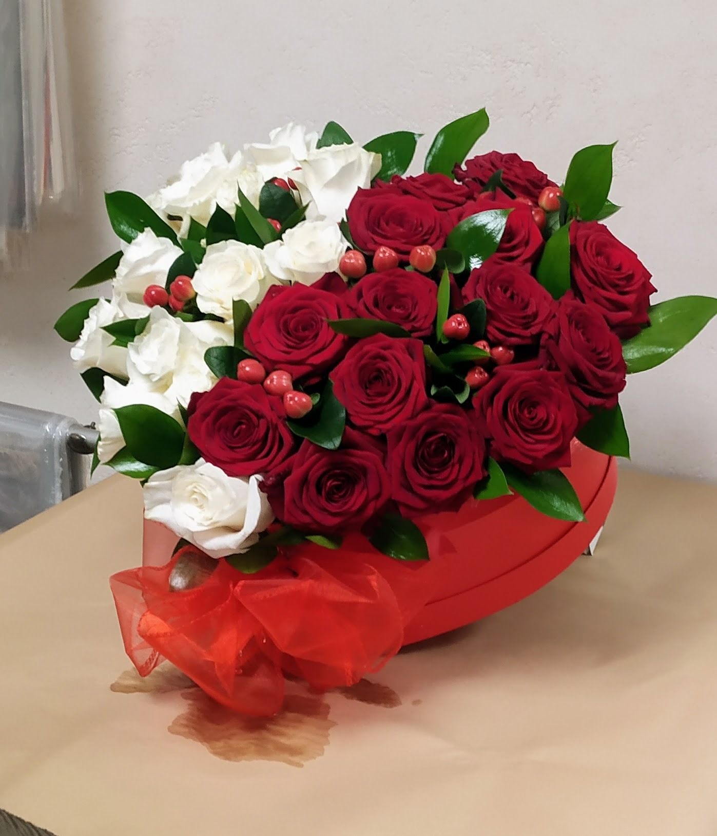 Kompozycja kwiatowa z czerwonych i białych róż w czerwonym, okrągłym pudełku z czerwoną, tiulową wstążką.