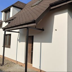 Złota rączka - Jasna elewacja domu jednorodzinnego z brązowym dachem i stolarką okienną, widok z boku na tle zieleni. Nowoczesne wykończenie, boczny widok.