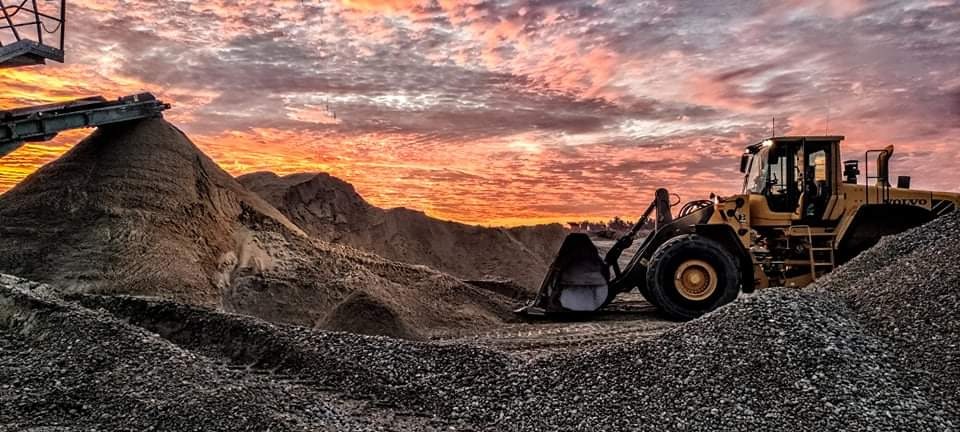 Żółta ładowarka Volvo na tle zachodzącego słońca w Żukowie, obok hałda gruzu i przesiewacz.