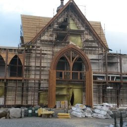 MARGAB STOLARSTWO OGÓLNE MARCIN CEREMON - Konstrukcja budynku z drewnianym szkieletem w trakcie montażu, widoczne rusztowania, okna w stylu gotyckim i materiały budowlane na placu budowy.