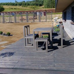 MARGAB STOLARSTWO OGÓLNE MARCIN CEREMON - Drewniany taras z szarą, nowoczesną grupą mebli ogrodowych, w tle trawnik i ogrodzenie z suszącym się praniem.