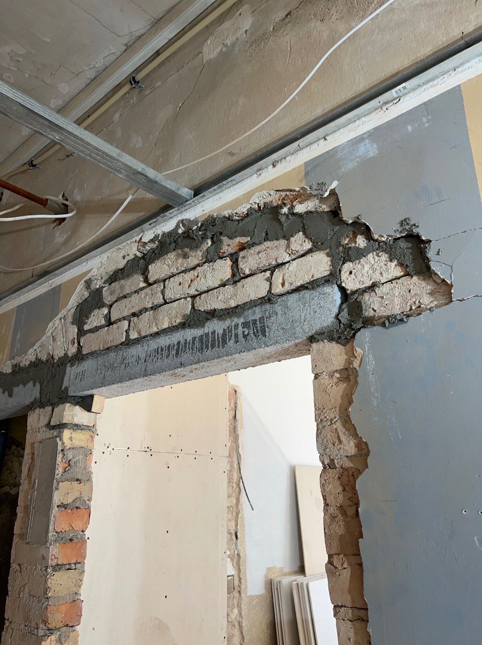 Wzmocnienie nadproża nad otworem drzwiowym z widoczną konstrukcją z cegieł i zaprawy, częściowo obudowane płytą kartonowo-gipsową, z metalową konstrukcją sufitu podwieszanego w tle.