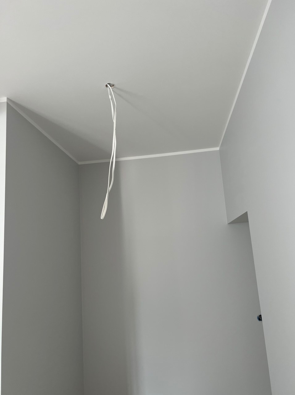 Świeżo pomalowane szare ściany w pokoju z białym obramowaniem sufitu i wystającymi kablami z otworu w suficie.