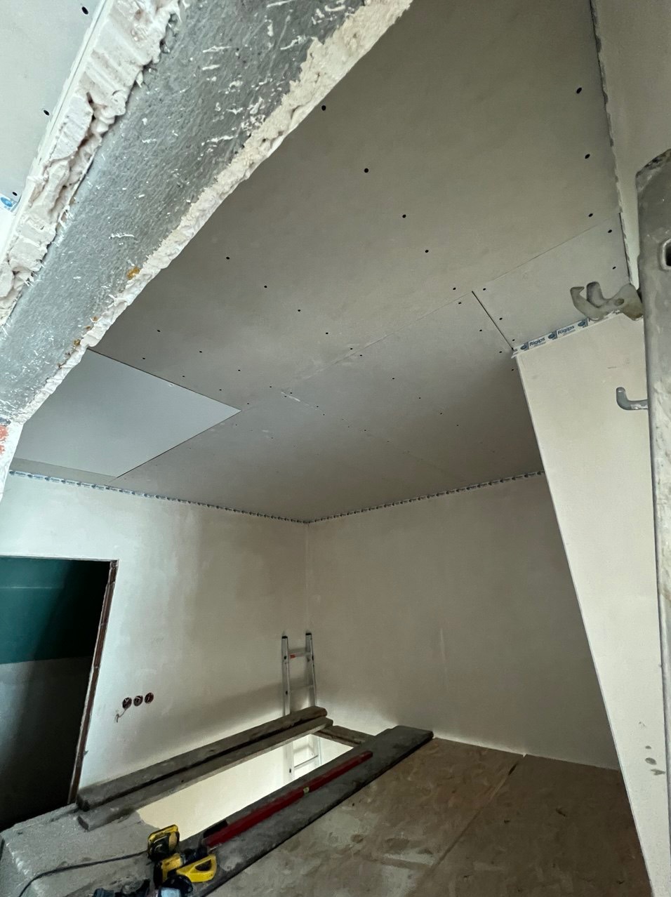 Wnętrze w trakcie montażu płyt kartonowo-gipsowych na suficie i ścianach, widoczna konstrukcja nośna, szpachlowane łączenia, oraz narzędzia na podłodze.