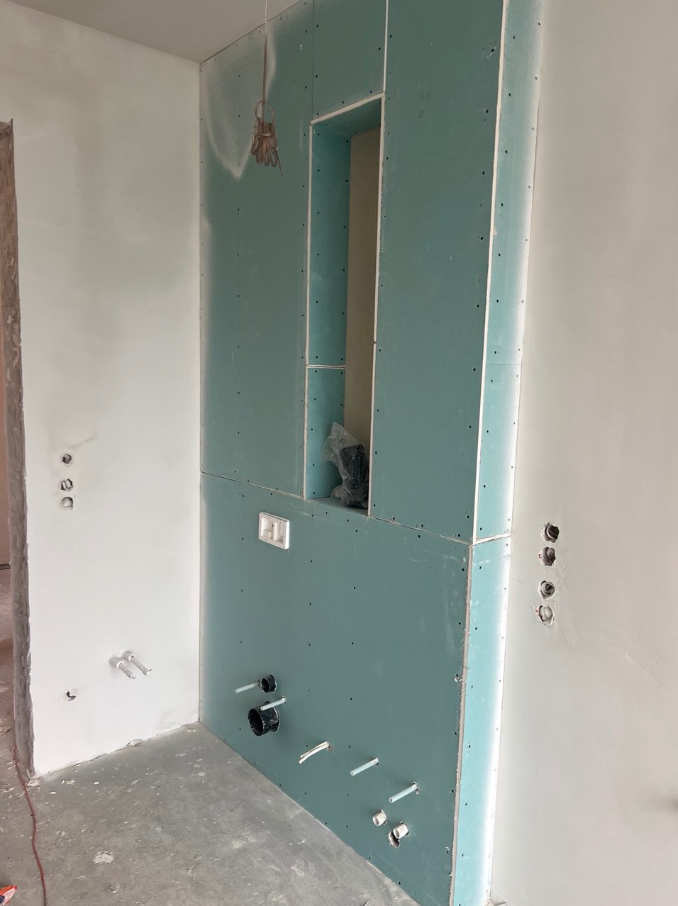 Ściana z płyty karton gips z wnęką i wyprowadzonymi instalacjami wodno-kanalizacyjnymi oraz elektrycznymi w surowym stanie.