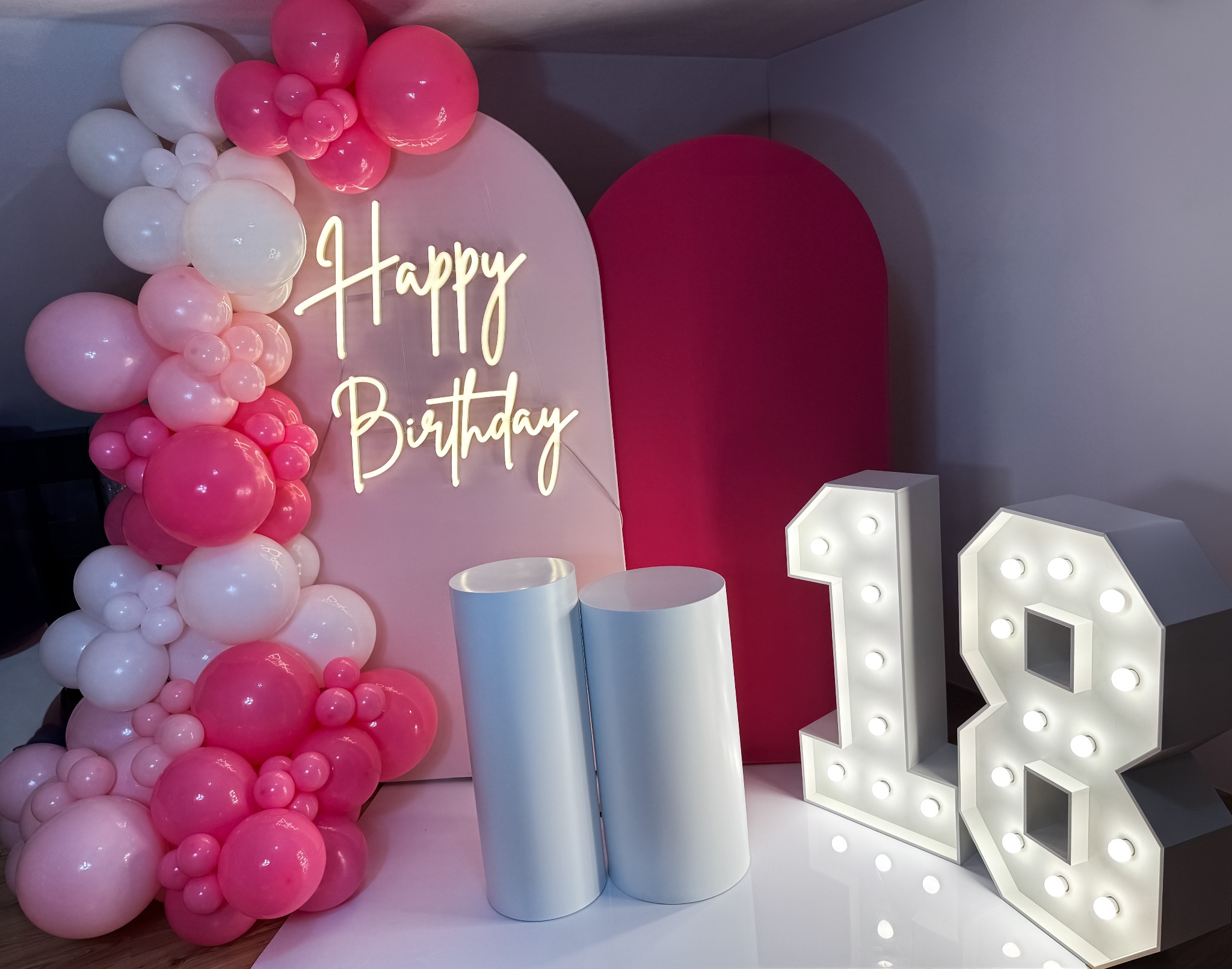 Dekoracja urodzinowa na osiemnaste urodziny: girlanda z różowych i białych balonów, podświetlany napis 'Happy Birthday' oraz cyfry '18' z żarówkami.