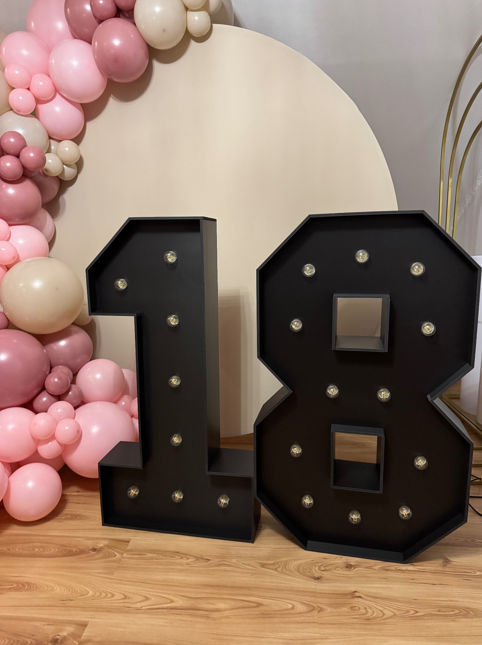 Dekoracja urodzinowa: podświetlane cyfry '18' w czarnej oprawie, pastelowa girlanda balonowa w odcieniach różu i beżu oraz okrągłe tło.