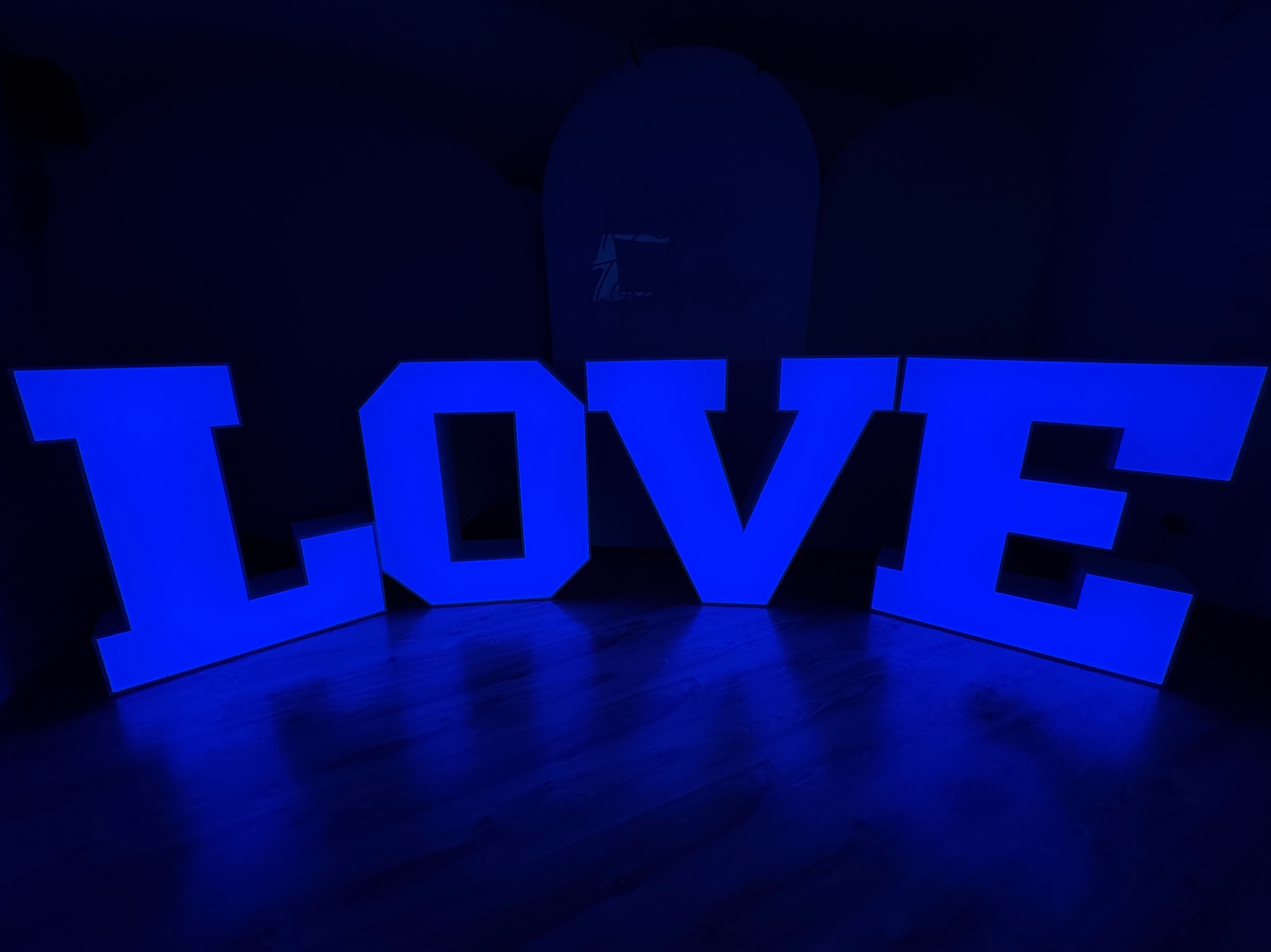 Podświetlany na niebiesko napis LOVE, dekoracja na imprezę, ustawiony na ciemnej podłodze, widoczne odbicia światła.