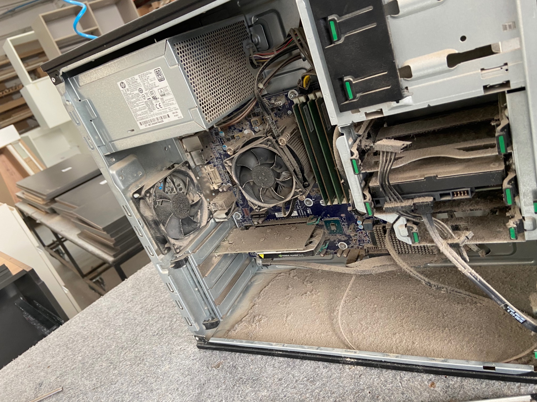 Wnętrze zakurzonego komputera stacjonarnego HP z widoczną płytą główną, wentylatorami, zasilaczem i kartą graficzną Nvidia Quadro K420.