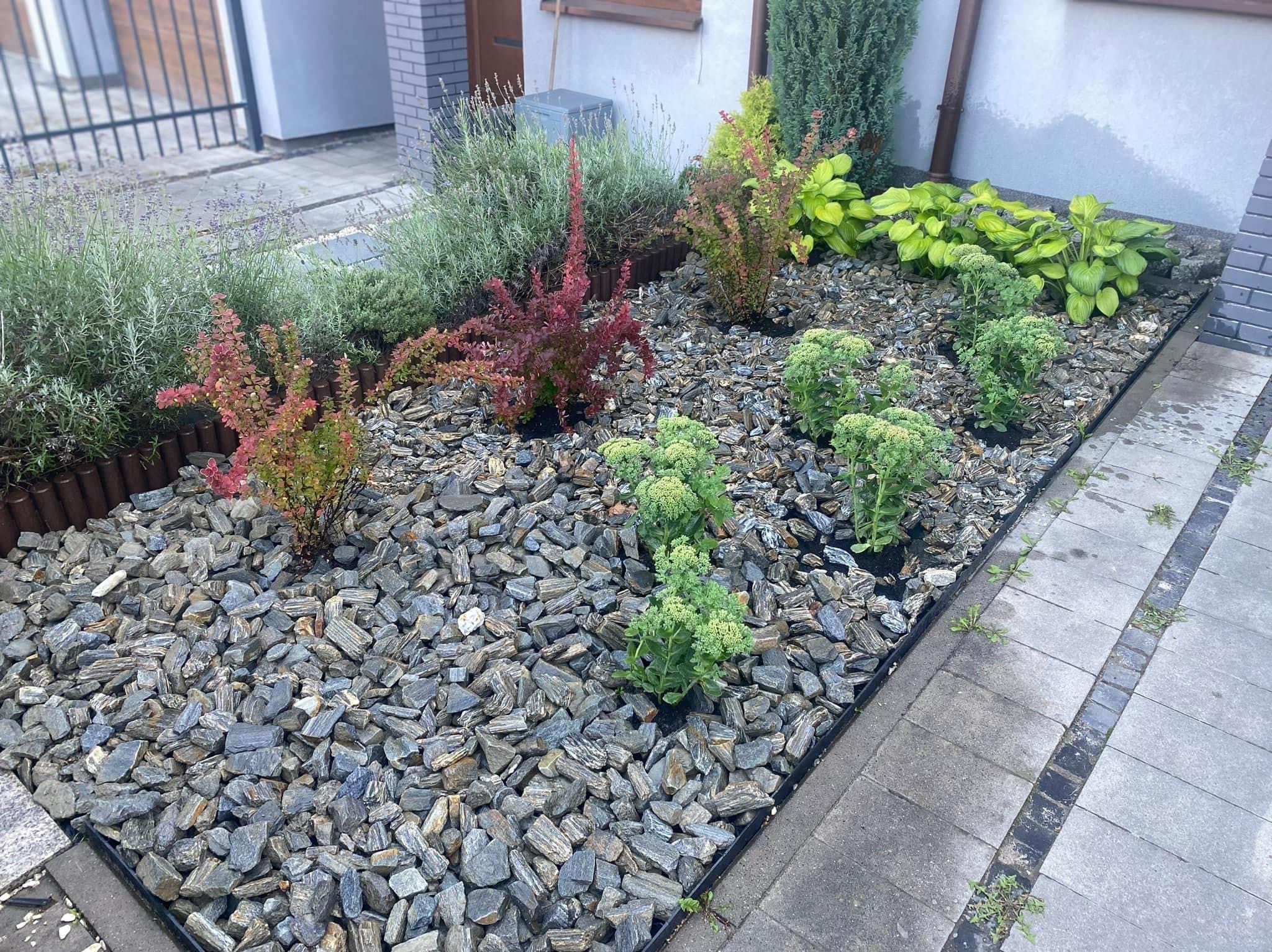 Ogród przed domem z roślinami ozdobnymi, wysypany grysem, obrzeża z palisady i kostki, widok z góry.