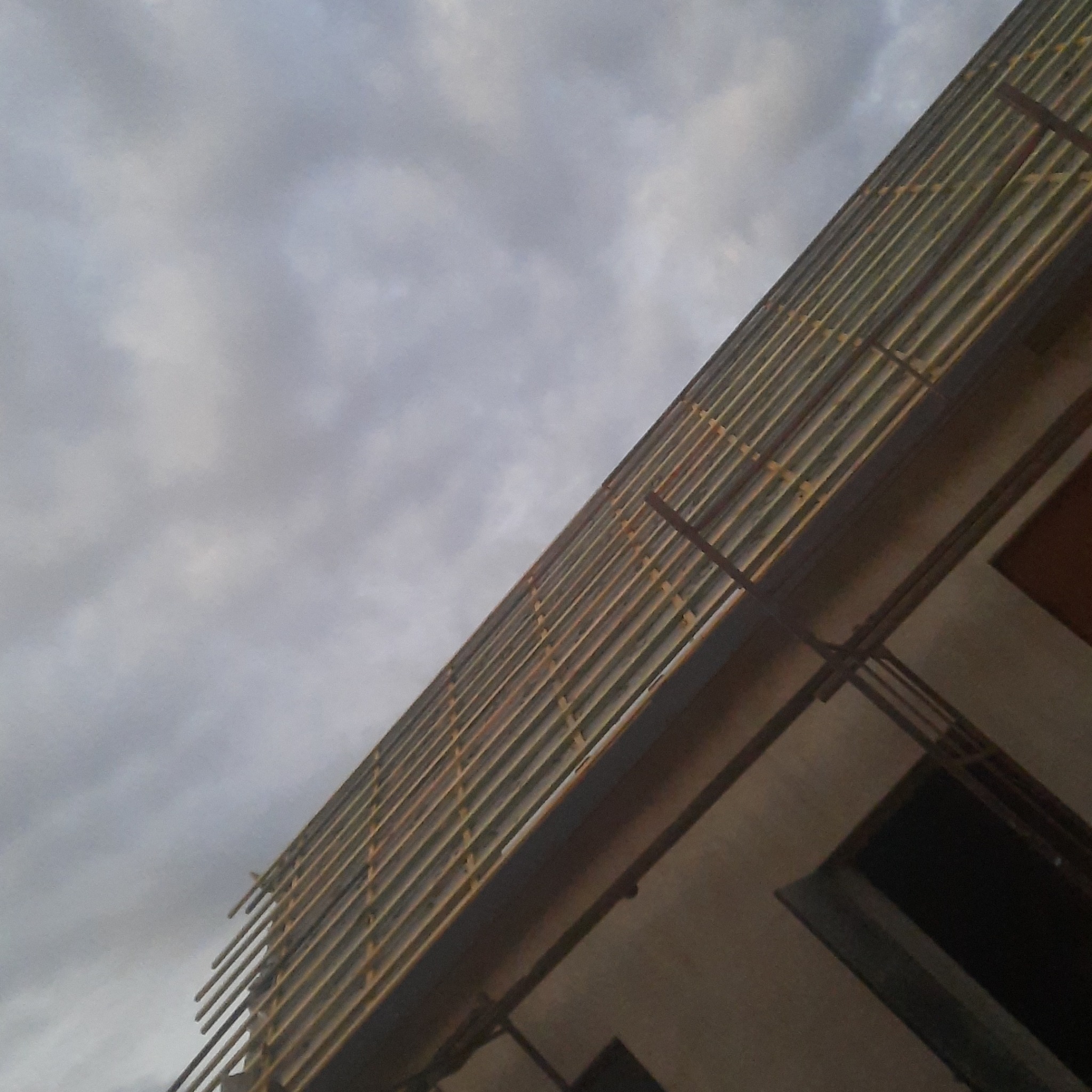 Skośny widok na konstrukcję dachu z łatami i kontrłatami na tle pochmurnego nieba.
