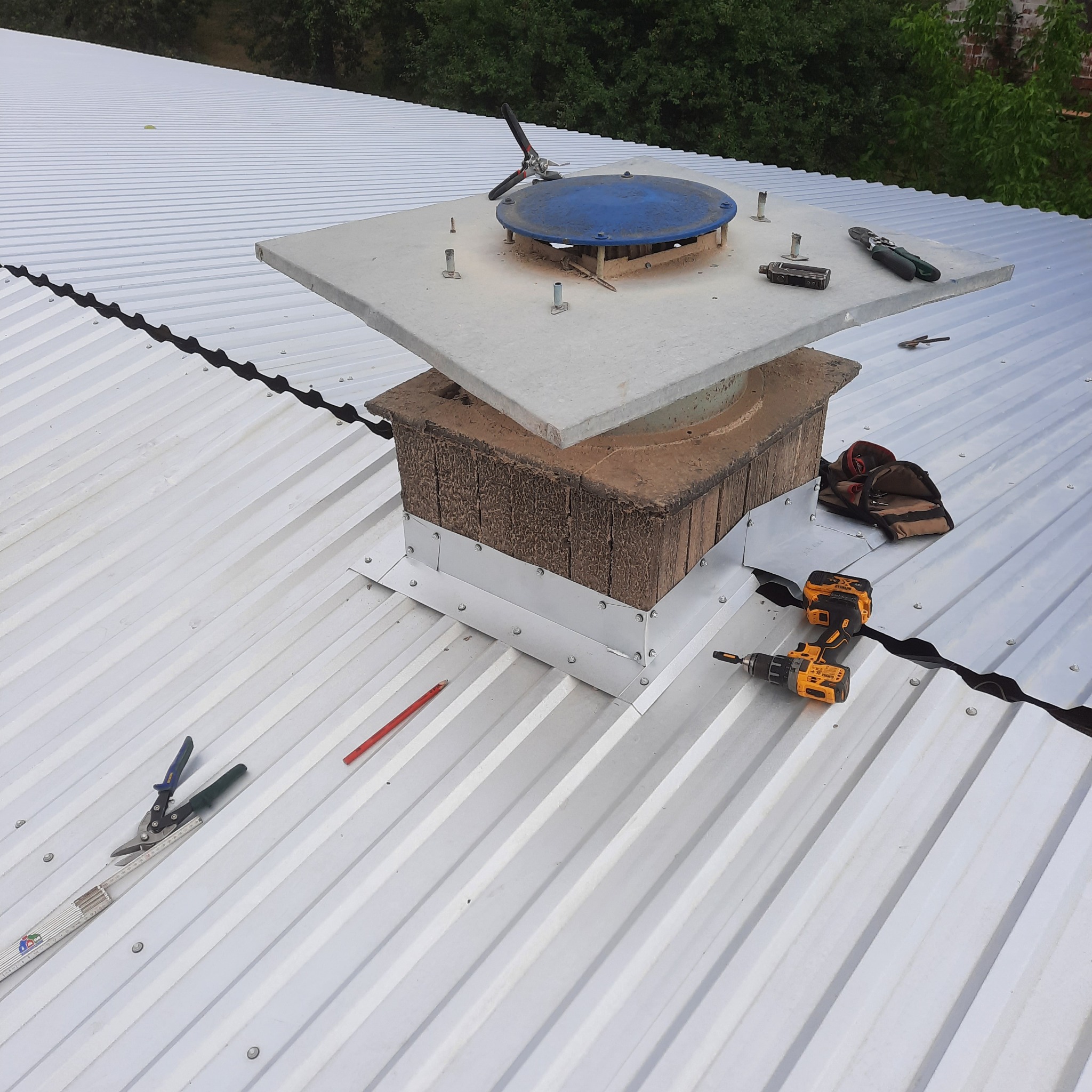 Montaż kominka wentylacyjnego na dachu z blachy trapezowej, widoczne narzędzia i wkrętarka.
