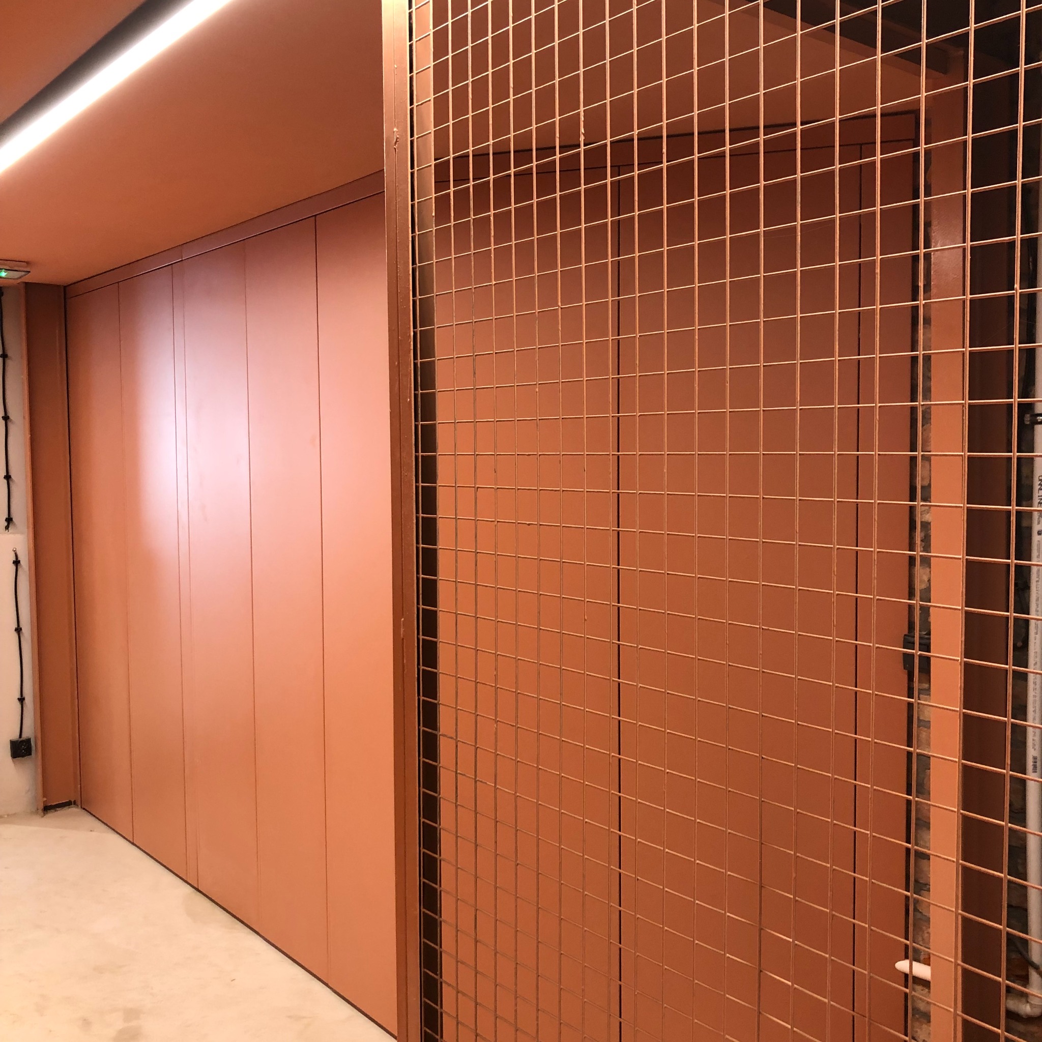 Pomarańczowa szafa w zabudowie z metalową kratą w minimalistycznym wnętrzu.