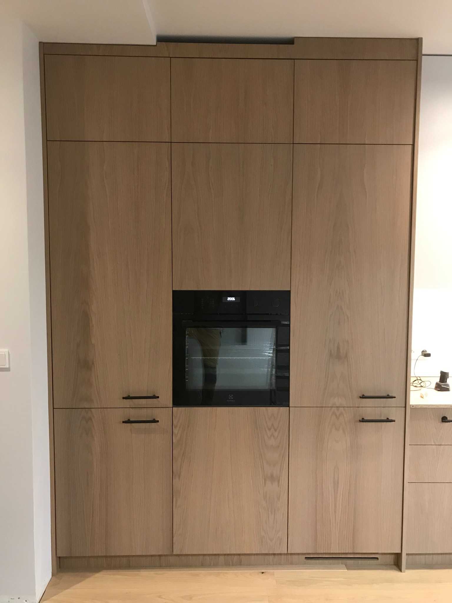 Jasne, drewniane szafki kuchenne na wymiar z wbudowanym piekarnikiem Electrolux i minimalistycznymi, czarnymi uchwytami.