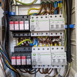 Magdalena WOJTAROWICZ- MAPI - Otwarta skrzynka elektryczna z zainstalowanymi zabezpieczeniami przepięciowymi Phoenix Contact Valvetrab, wyłącznikami nadprądowymi Noark oraz przewodami w różnych kolorach, widoczne oznaczenia L1,...