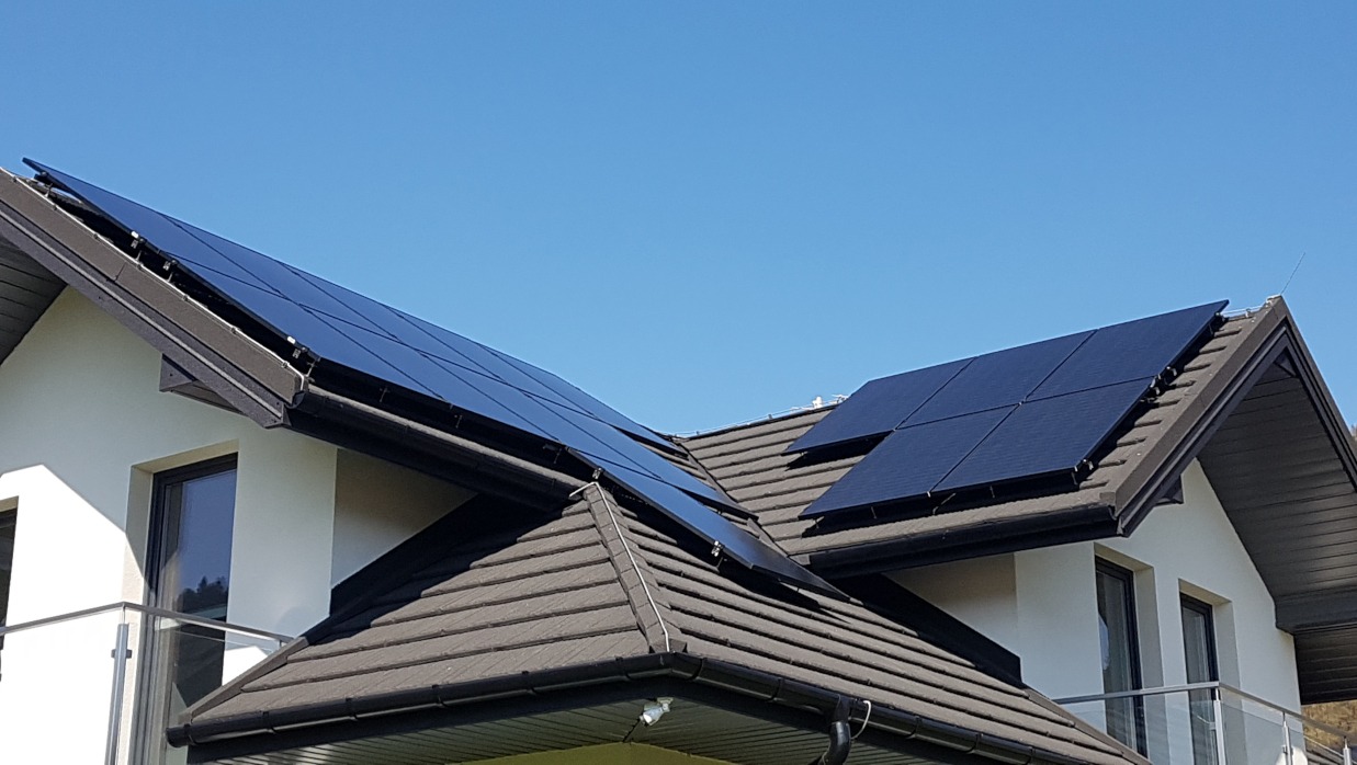 Nowoczesny dom jednorodzinny z panelami słonecznymi na dachu pokrytym szarą dachówką, Krościenko nad Dunajcem, błękitne niebo w tle.