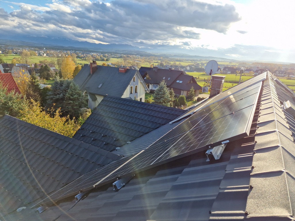 Panele fotowoltaiczne zamontowane na dachu domu z widokiem na Nowy Targ i góry w tle.