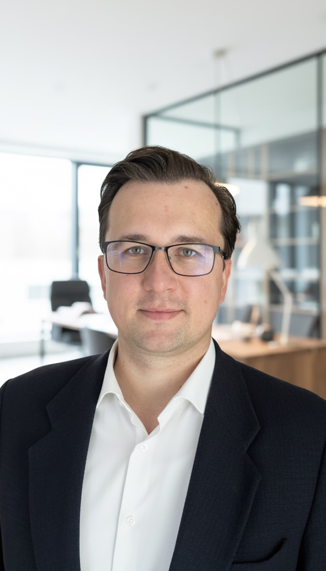 Portret mężczyzny w okularach i marynarce na tle biura. Uśmiechnięty prawnik w jasnym pomieszczeniu z przeszklonymi ścianami.