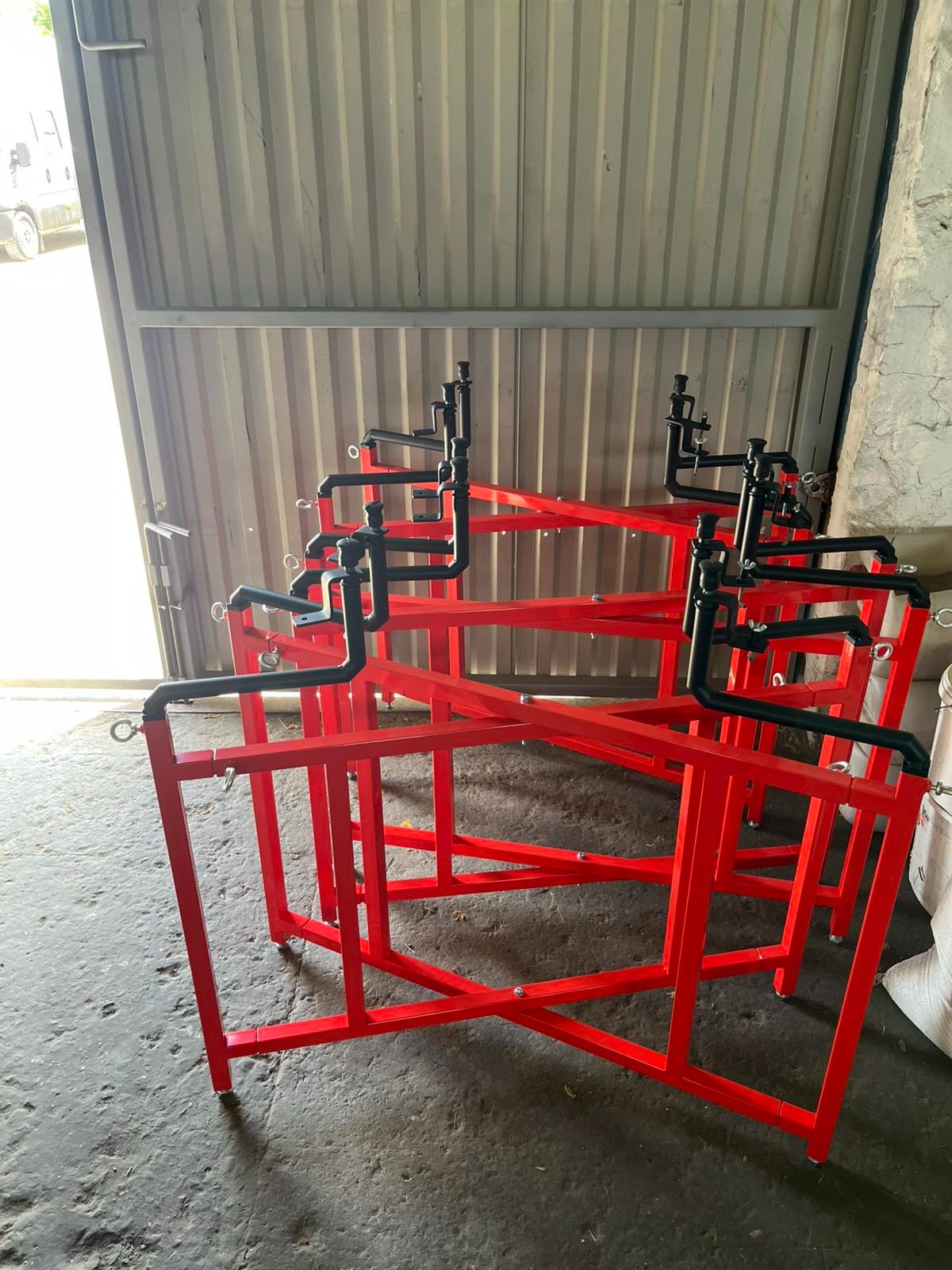 Czerwone, metalowe konstrukcje z czarnymi elementami rurowymi, ustawione w magazynie. Widoczne spawy i mocowania.