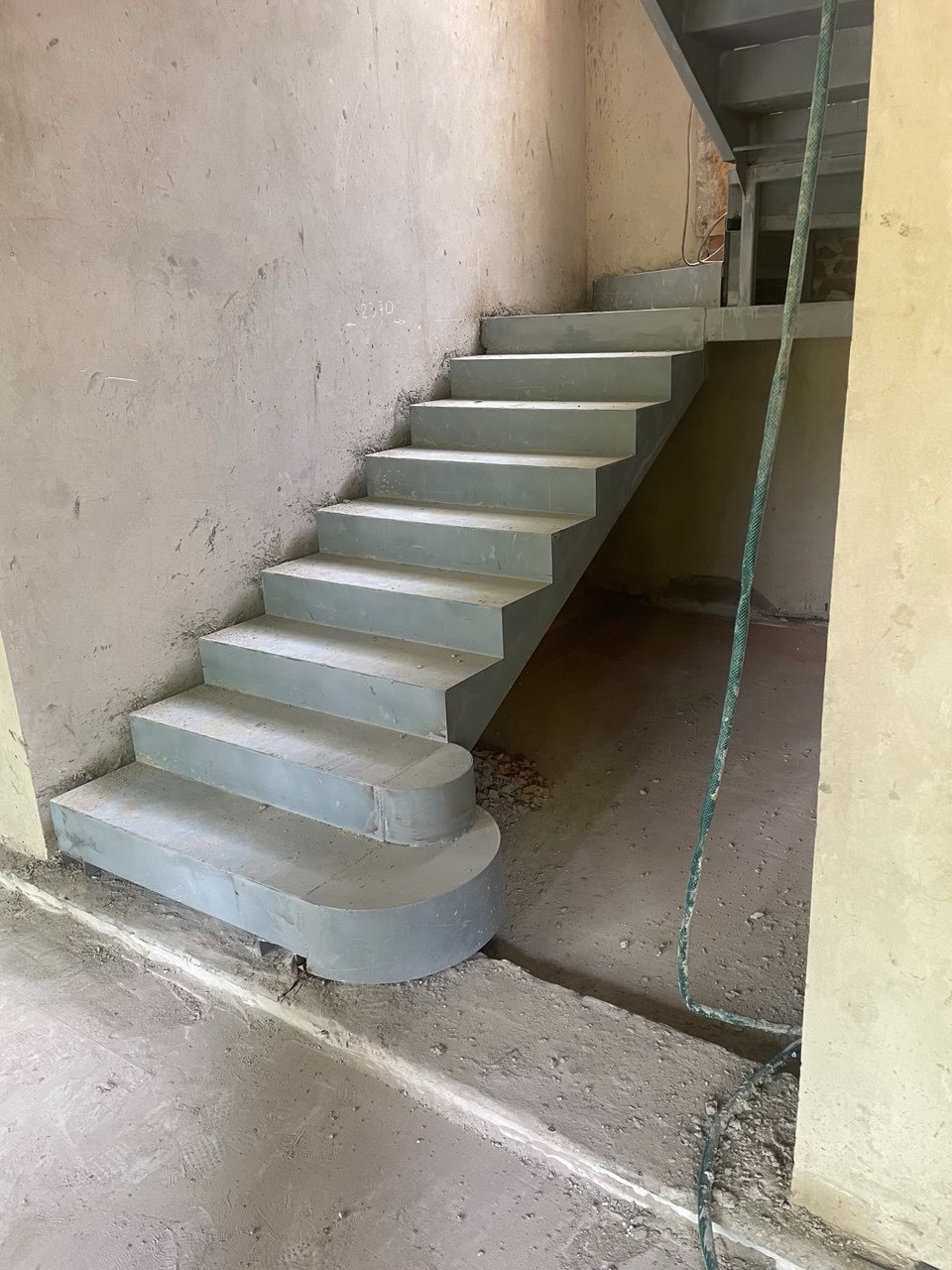 Surowe, betonowe schody wewnętrzne z zaokrąglonym pierwszym stopniem, prowadzące na antresolę w trakcie budowy. Widoczne ślady zaprawy i niedokończone ściany.