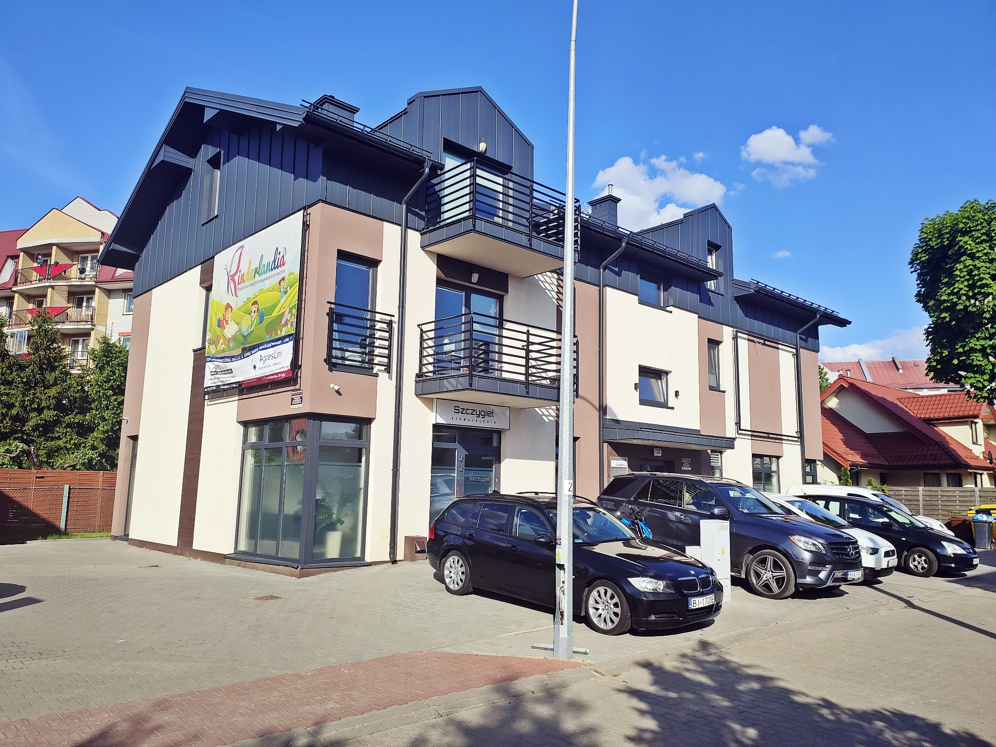 Elewacja budynku z szyldem 'Szczygieł Stomatologia' w Białymstoku, zaparkowane samochody, nowoczesna architektura, błękitne niebo.