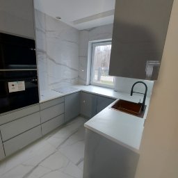 DM Invest Damian Zaremba - Nowoczesna kuchnia z szarymi frontami, białym blatem i marmurową ścianą oraz podłogą, z czarną armaturą i miedzianym zlewem.