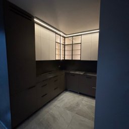 DM Invest Damian Zaremba - Nowoczesna kuchnia z szarymi frontami szafek dolnych i białymi górnymi szafkami z czarnymi ramkami, oświetlenie LED pod szafkami górnymi, szara podłoga z płytek.