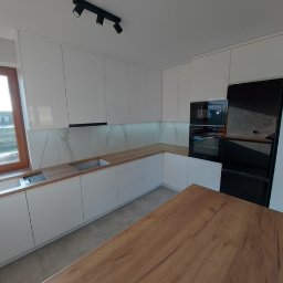 DM Invest Damian Zaremba - Nowoczesna kuchnia z białymi szafkami, drewnianym blatem i wyspą, oświetleniem punktowym na suficie i marmurowym panelem ściennym.