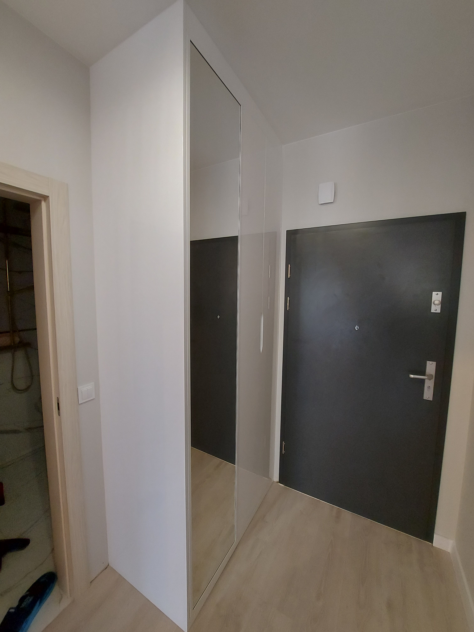 Biała szafa wnękowa z lustrzanymi drzwiami w przedpokoju, widoczna czarna ściana w odbiciu lustra