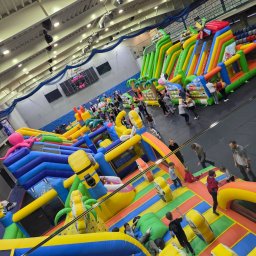 DAGMARA BARWIŃSKA-TRZECIAK RATOWNIK MEDYCZNY - Wielki, kolorowy park rozrywki z dmuchanych atrakcji w hali sportowej, z widocznymi dziećmi i dorosłymi korzystającymi z konstrukcji.