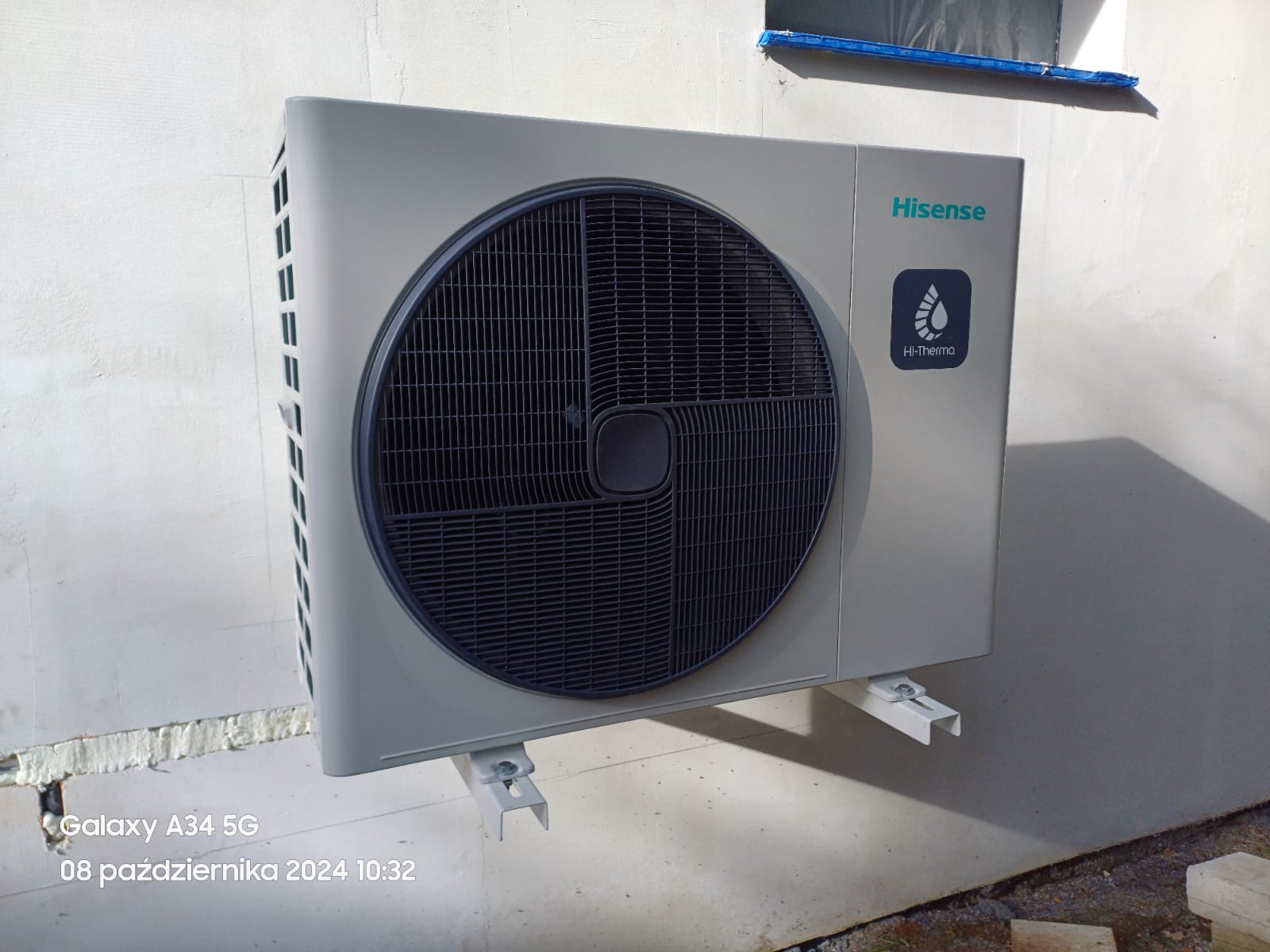 Zewnętrzna jednostka pompy ciepła Hisense zamontowana na białej ścianie, widoczne wsporniki montażowe i logo Hi-Thermo.
