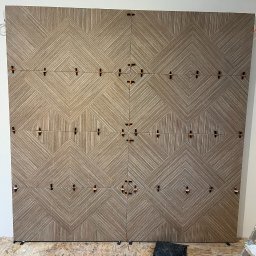 PRIMEBUD NAZAR KACHAK - Układanie dekoracyjnych, brązowych płytek ściennych z użyciem klipsów poziomujących. Widoczna drabina i podłoga w trakcie prac wykończeniowych.