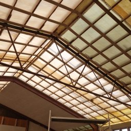 Łukasz Słonina - Konstrukcja dachu od wewnątrz z widocznym ociepleniem między krokwiami, rusztowanie i pracownik w tle.