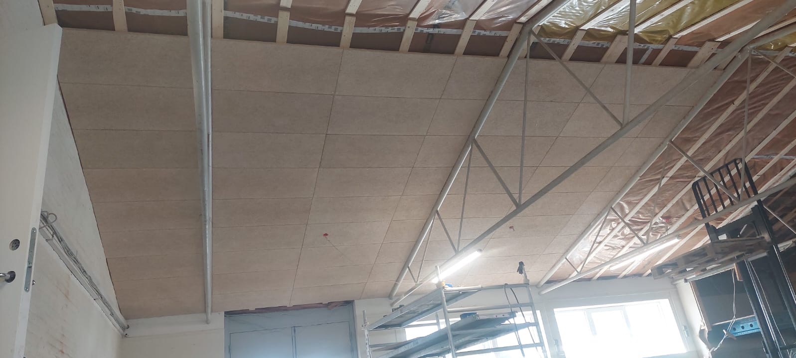 Montaż płyt na poddaszu z widoczną konstrukcją dachu i ociepleniem od góry, w tle rusztowanie.