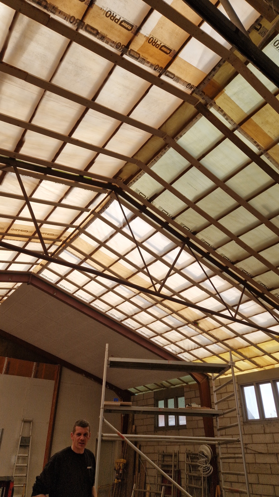 Konstrukcja dachu od wewnątrz z widocznym ociepleniem między krokwiami, rusztowanie i pracownik w tle.