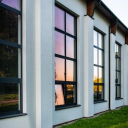 BOGDAŃSKI SPÓŁKA JAWNA JAN I CZESŁAW BOGDAŃSCY - Elewacja budynku z rzędem okien z czarnymi ramami, w których odbija się zachód słońca, podkreślona przez pionowe elementy architektoniczne.