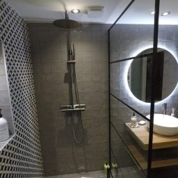 Klusbedrijf Ceasar - Nowoczesna łazienka w odcieniach szarości z kabiną prysznicową typu walk-in, okrągłym lustrem z podświetleniem LED i umywalką nablatową na drewnianym blacie.
